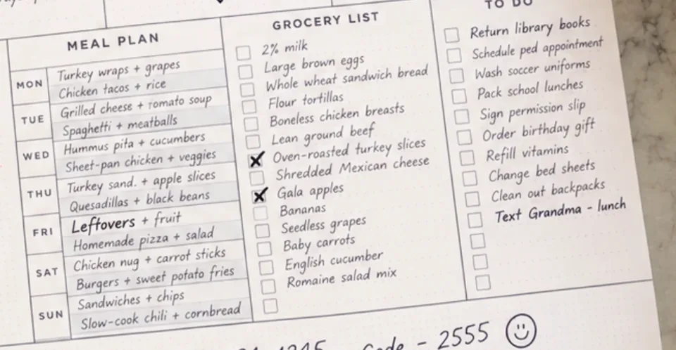 Close-up of the wall calendar’s meal plan and grocery list: meals written for each day of the week, from turkey wraps and chicken tacos on Monday to slow-cook chili on Sunday, and a grocery list with milk, eggs, tortillas and chicken breasts.