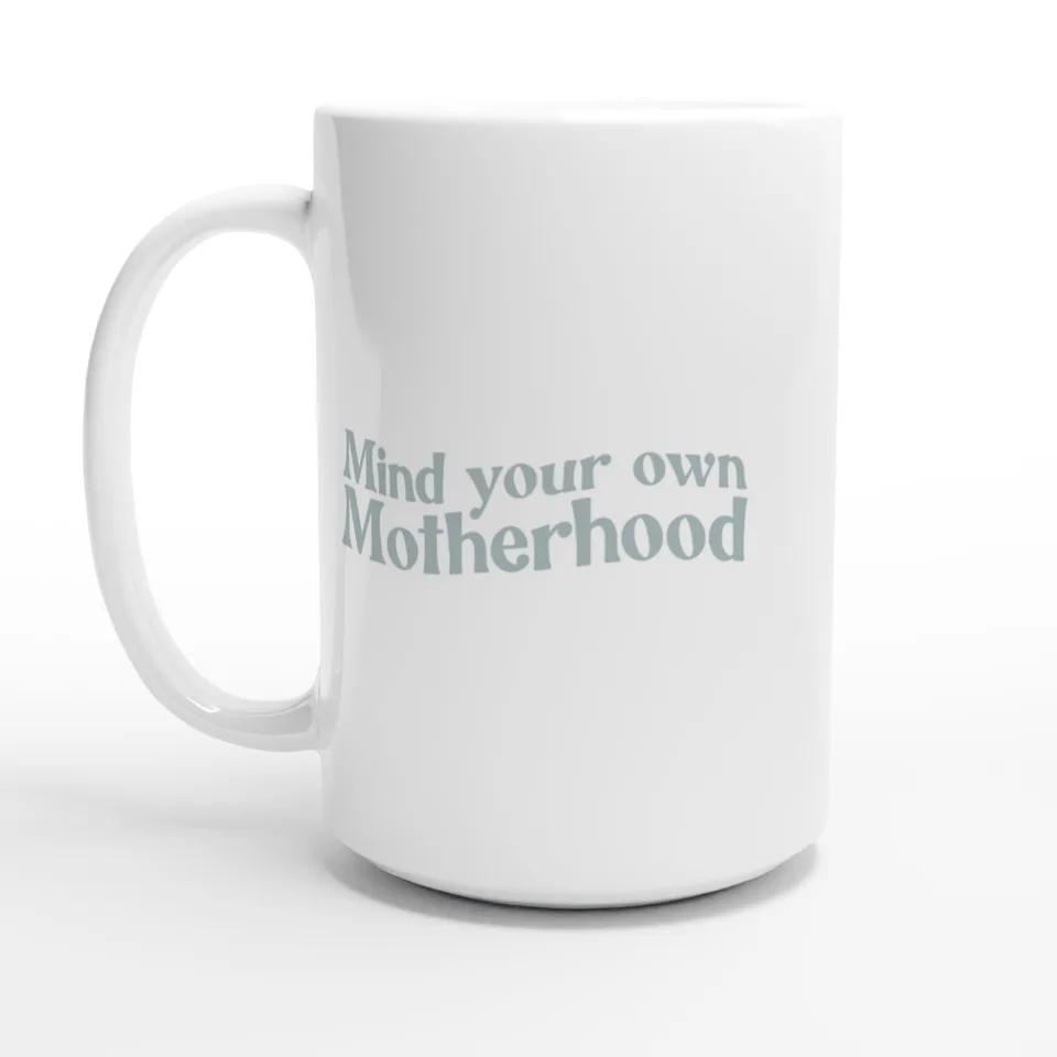A white 15oz ceramic mug printed with “Mind your own Motherhood” in soft sage-gray lettering.